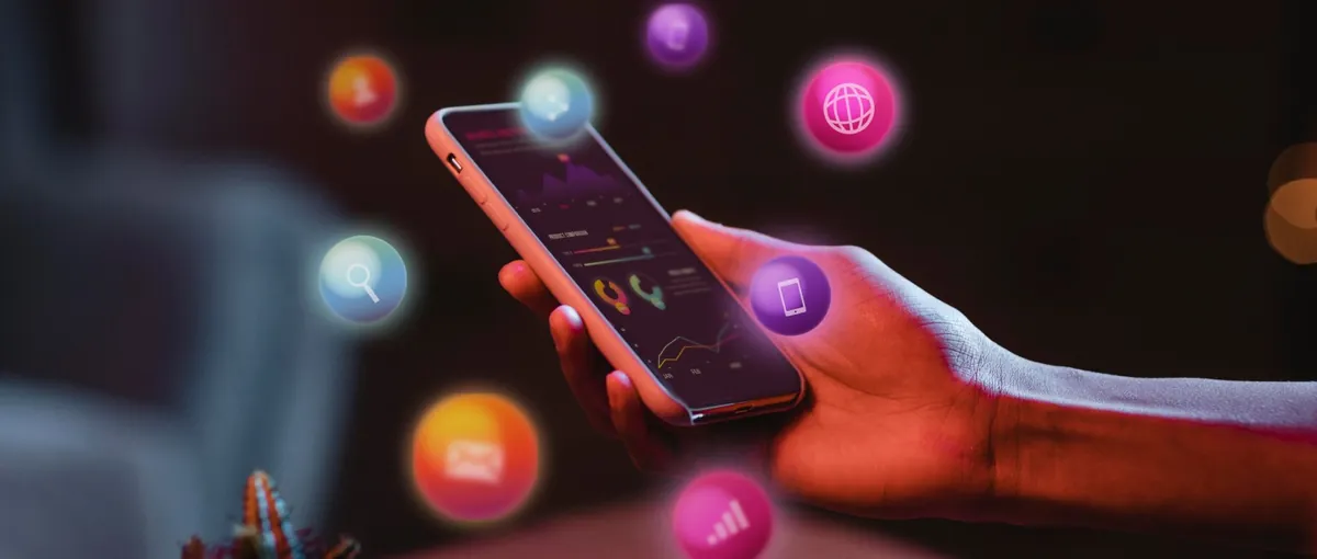 Hand holding a smartphone surrounded by floating app icons for search, messaging, web and analytics